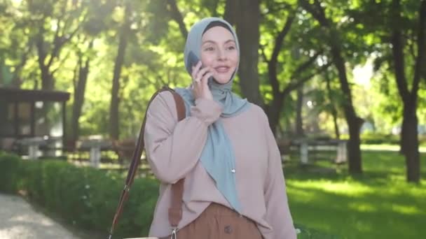 Muslim Woman Walks Park Wearing Hijab Using Mobile Phone Smiling — Stockvideo