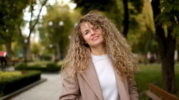 도시의 공원에 곱슬머리의 카메라 앞에서 장난기있게 명랑하고 귀여운 여자의 아름다운 — 비디오