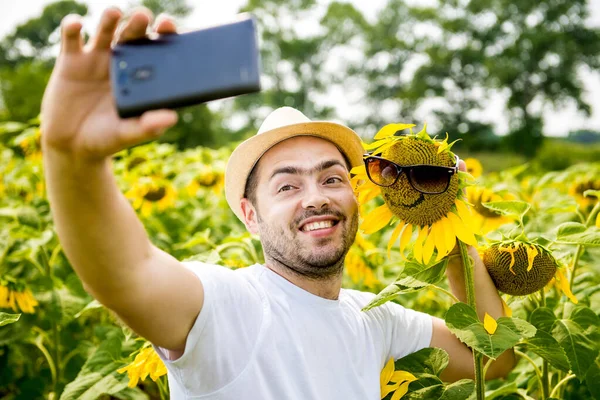 Adam selfie ayçiçeği tarlası üstünde a hareket eden telefon fotoğraf makinesi yapar.