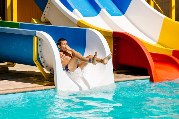 A little boy slides down a water slide and has fun. The boy swims in the pool after going down the water slide in summer.