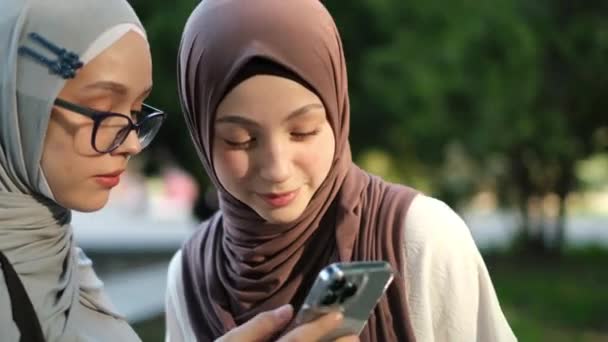 Δύο Νεαρές Μουσουλμάνες Φορούν Χιτζάμπ Περπατούν Στο Πάρκο Χρησιμοποιούν Smartphone — Αρχείο Βίντεο