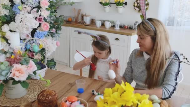 一个可爱的小女孩和她的妈妈坐在厨房的桌子旁 手里拿着一只兔子 庆祝复活节的装饰 — 图库视频影像