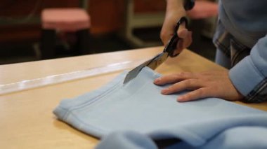 Giysi tamirhanesinde kadın terzi atölyede pantolon kesmek için makas tutuyor..