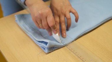 Giysi tamir atölyesinde çalışan bir kadın terzi atölyede pantolon kesmek için tebeşirle ölçü alır..