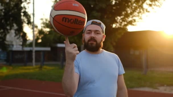ストリートフィールドで遊んでいる間 バスケットボール選手が指でバスケットボールを回転するのを見ているひげ付き男 スローモーション クライメンチョッグ ウクライナ 2023 — ストック動画