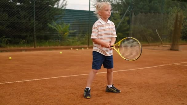 小さな子供がラケットでボールを打つことを学ぶ きれいな屋外でスポーツフィールドでテニスをすることを学ぶ 夏のアクティビティ — ストック動画