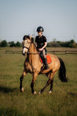 Kasklı genç bir çocuk yazın ata binmeyi öğrenir. Eğitmen çocuğa binicilik öğretir..