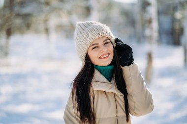 Güneşli bir günde kış parkında durup gülümseyen güzel bir kızın portresi. Kış tatili. Boşluğu kopyala.