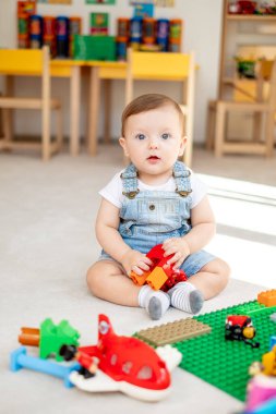 Kameraya bakıp, oyun odasında oyuncak otobüsle oynayan sevimli bir bebek.