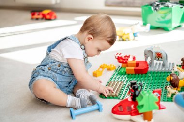 Kameraya bakıp, oyun odasında oyuncak otobüsle oynayan sevimli bir bebek.