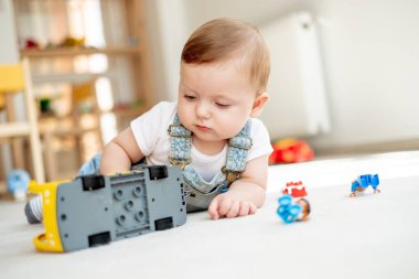 Kameraya bakıp, oyun odasında oyuncak otobüsle oynayan sevimli bir bebek.