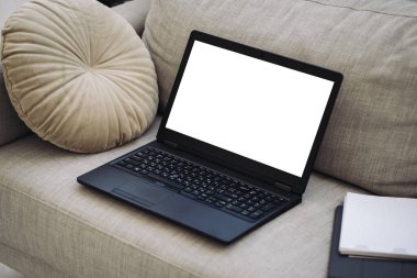 Boş ekranlı dizüstü bilgisayar, kalemli not defteri, kanepede duruyor.