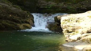 Nehir kıyısı boyunca yavaş çekimde akan bol miktarda suyun yakın çekimi. Dağlardaki akan nehir suyunun güzel manzarası. Yaz dağında küçük bir şelale sıçradı..