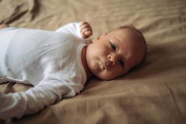 Annelik ve ebeveynlik. Kahverengi yatakta uzanan sevimli bir oğlan çocuğu. Beyaz bebek kıyafetinin içinde yeni doğmuş şirin bir bebek. Evlat edinme ve doğurganlık kavramı