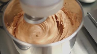 Bir stand mikser paslanmaz çelik bir kasede pürüzsüz bir hamur yoğurur ve profesyonel bir mutfakta süreci gözler önüne serer. Kremalı karışım, taze malzemeler kullanarak pişirme sanatının bir örneği..