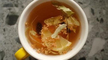 Limon dilimleri ve kurumuş çiçeklerle dolu beyaz bir fincan bitki çayı. Rahatlatıcı, canlandırıcı sıcak bir içecek..