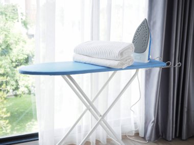 Elektrikli buhar ütüsü ve ütü masasında giysi yığını
