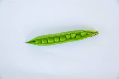 Yeşil bezelyeler bir vazoda toplanır ve bezelye kabukları beyaz arka planda onun yanındadır.