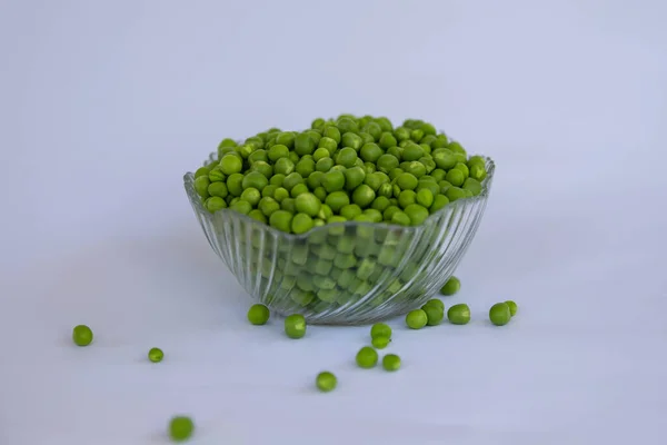 green peas are piled in a vase and pea pods are next to it on a white background
