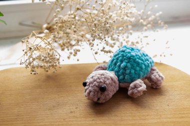 knitted blue-violet turtle with a bouquet of flowers on the background of the window