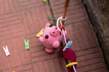 a knitted pink pig hangs things on clothespins