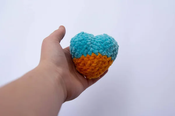 a knitted yellow-blue heart is held by a child