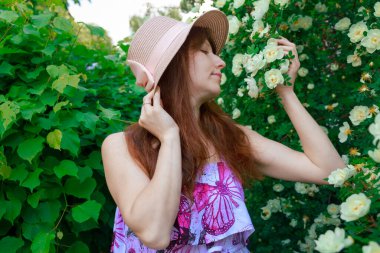 Şapkalı ve elbiseli bir kız, bir çalılık beyaz güller, bir çay gülü 