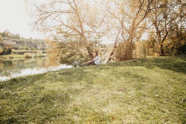 Kız gölün kıyısında oturuyor, güneş parlıyor, sonbahar.