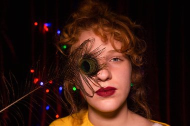 Bir kız tavus kuşu tüyüyle poz verir.