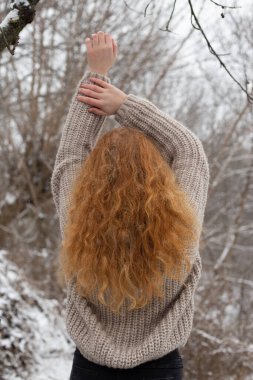 Kızıl saçlı kız kışın kolları havada bir kazakla ayakta duruyor.