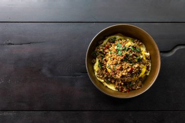 Tahta zeminde duran fesleğenli pirinçli kıymalı domuz eti.