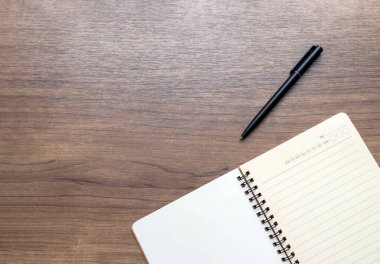Yukarıdan ahşap bir masa, açık bir defter ve kalem. Boş beyaz arkaplan ve metin için boşluk. en üstteki görünüm