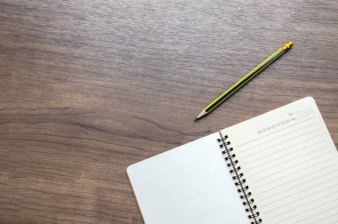 Yukarıdan ahşap bir masa, açık bir defter ve kalem. Boş beyaz arkaplan ve metin için boşluk. en üstteki görünüm
