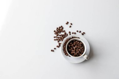 Saf beyaz arka planda sıcak kahve ve fasulye kaynayan bir fincanın yakın çekimi. Koyu kahve çekirdeklerinin aromatik karışımı güne başlamak için nefis bir uyanış vadediyor.