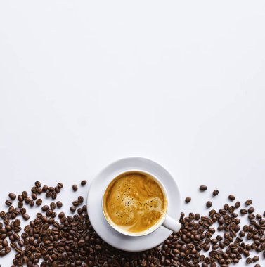 Saf beyaz arka planda sıcak kahve ve fasulye kaynayan bir fincanın yakın çekimi. Koyu kahve çekirdeklerinin aromatik karışımı güne başlamak için nefis bir uyanış vadediyor.