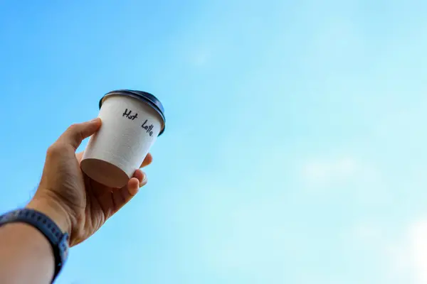 hand holding paper cup of coffee with blue sky background
