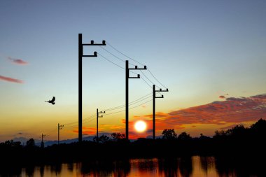 Enerji ve doğa temalı projeler için mükemmel, canlı bir günbatımına karşı siluetlenmiş yüksek voltaj direklerinin nefes kesici görüntüsü. 3B Görüntü