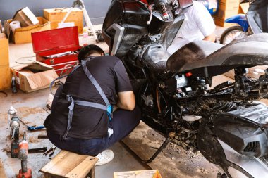 Bir tamirci, sel yüzünden hasar gören bir motosikleti tamir ediyor..
