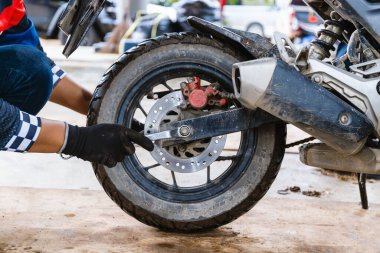 Motosikletin arka tekerleğinde tamirci, disk fren sistemini ayarlamaya odaklanıyor. Bu resim otomotiv onarım içeriği, teknik rehberler veya hizmet tanıtımları için mükemmeldir..