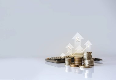 Artan faiz oranları, finansal büyüme ve yatırım fırsatlarını sembolize eden, yüzdelik büyüme okları ve hesap makinesi içeren birikmiş paralar.  