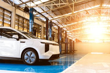Profesyonel bir oto tamirhanesinde, bakım ve teftiş için hidrolik asansörün altına yerleştirilmiş elektrikli bir araç..