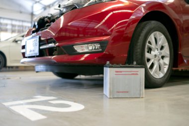 Kırmızı bir aracın yanındaki atölye zemininde araba aküsünün yakın çekimi..