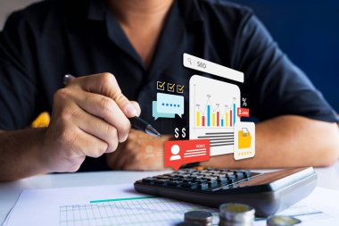 SEO ölçümlerini, finansal grafiklerini analiz etmek ve iş hedeflerine ulaşmak için hesap makinesi ve veri görselleştirme araçları kullanan bir işadamı.