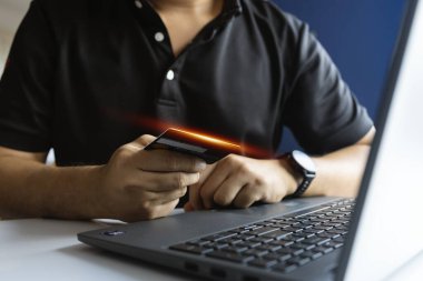 Adam kredi kartı ve laptop kullanarak güvenli bir ödeme yapıyor, dijital işlemleri, e-ticareti ve finansal teknolojiyi sembolize ediyor.