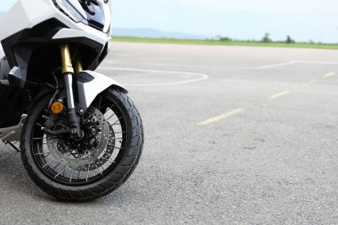 Ön tekere yakın çekim, süspansiyon ve disk frenleri. Macera motosikleti asfalta park edilmiş, modern motosiklet tasarımı ve ayrıntıları sergileniyor..