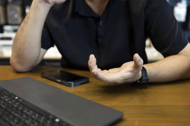 Siyah gömlekli bir adamın video görüşmesi sırasında telefon ve dizüstü bilgisayarla iletişim kurması, modern iş iletişimi kavramı..