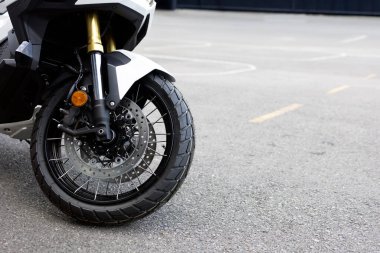 Ön tekere yakın çekim, süspansiyon ve disk frenleri. Macera motosikleti asfalta park edilmiş, modern motosiklet tasarımı ve ayrıntıları sergileniyor..