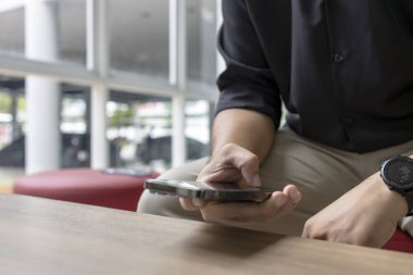 Modern kapalı alanda akıllı telefon kullanan bir adamın yakın çekimi. İş gündelik tarzı, rahatlatıcı, teknolojik yaşam tarzı, iletişim konsepti.