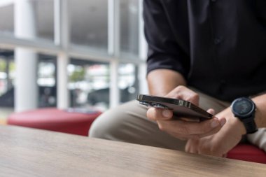 Modern kapalı alanda akıllı telefon kullanan bir adamın yakın çekimi. İş gündelik tarzı, rahatlatıcı, teknolojik yaşam tarzı, iletişim konsepti.