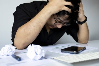 Finansal kağıtlar, buruşuk çarşaflar ve akıllı telefonlar ile çalışma masasında kafası karışmış bir adam.